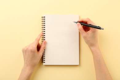 Photo of Woman writing in notebook on beige background, top view