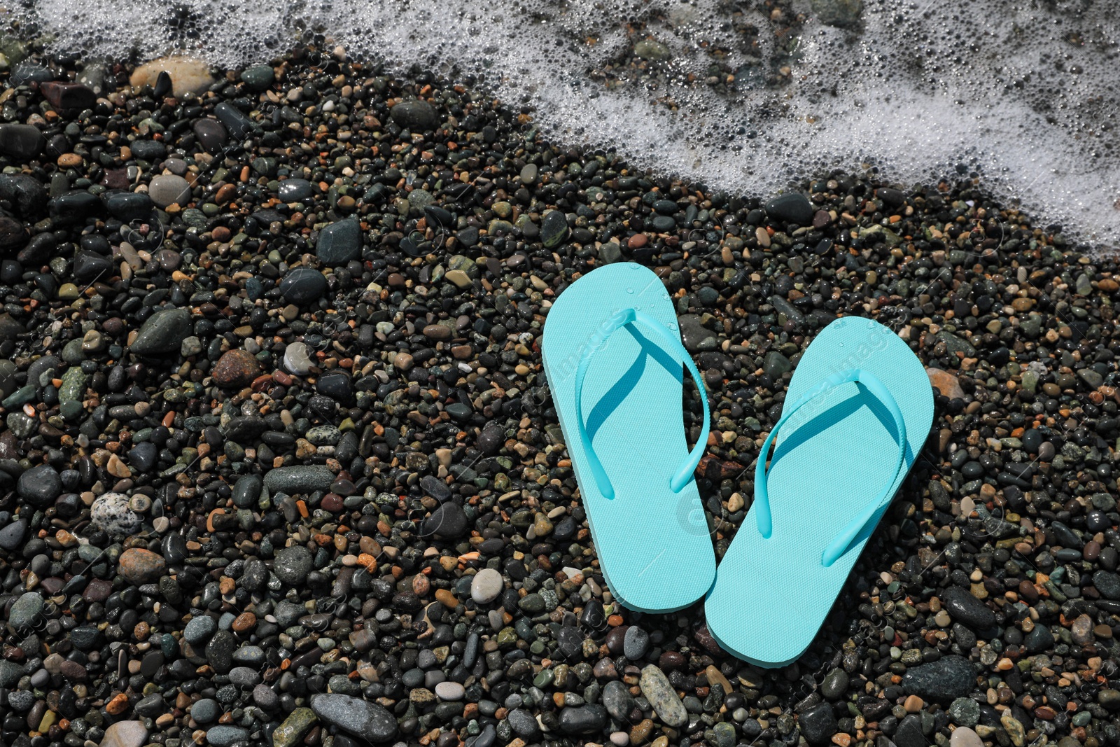 Photo of Stylish turquoise flip lops on pebble beach near beautiful sea wave, above view. Space for text