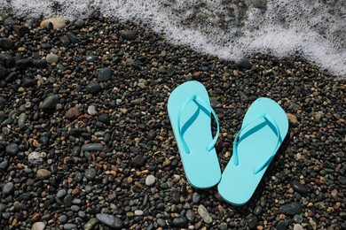 Photo of Stylish turquoise flip lops on pebble beach near beautiful sea wave, above view. Space for text