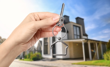 Image of Real estate agent holding key against modern house, closeup