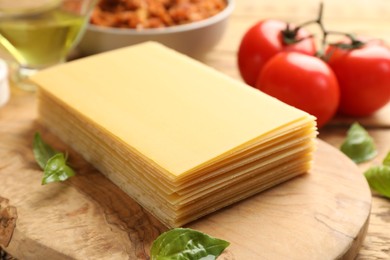 Photo of Cooking lasagna. Wooden board with pasta sheets and basil leaves on table, closeup