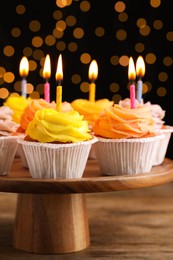 Photo of Stand with birthday cupcakes on wooden table against blurred lights, closeup