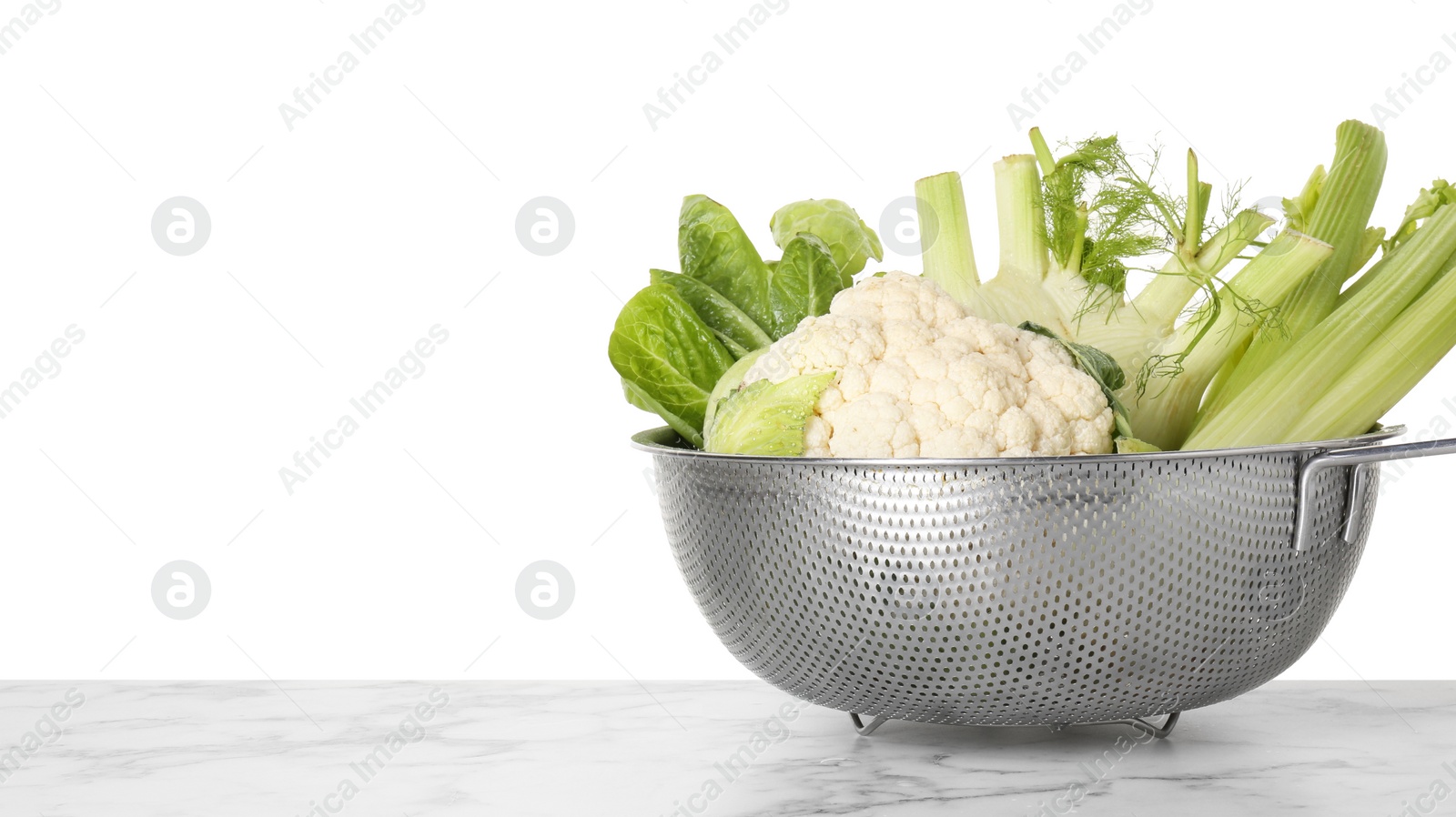 Photo of Metal colander with different vegetables on marble table against white background, space for text