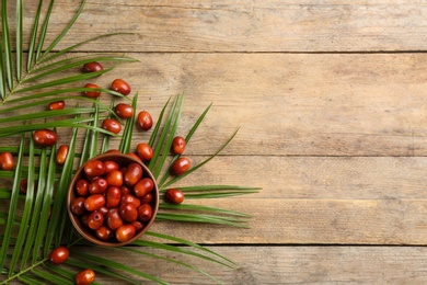 Palm oil fruits in bowl on wooden table, flat lay. Space for text