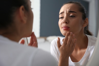 Photo of Young woman with herpes on lip looking in mirror at home