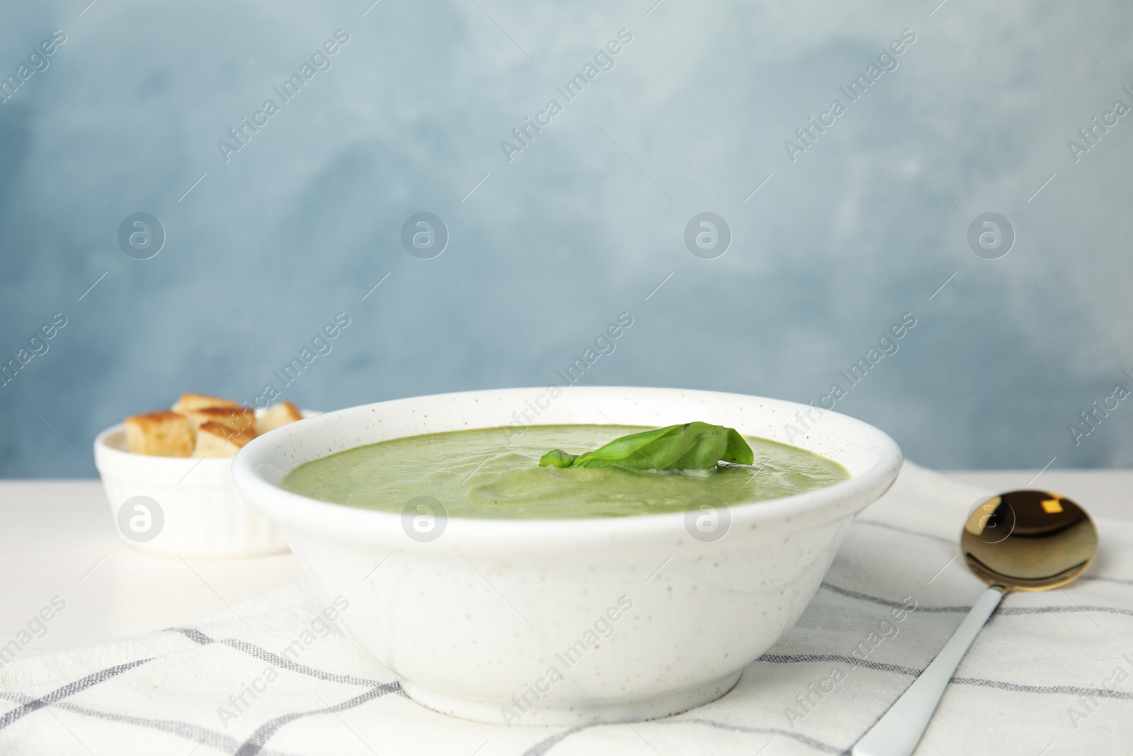 Photo of Delicious broccoli cream soup served on table against blue background. Space for text