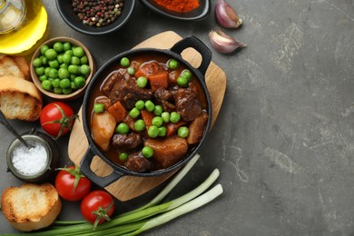 Photo of Delicious beef stew and ingredients on grey table, flat lay. Space for text