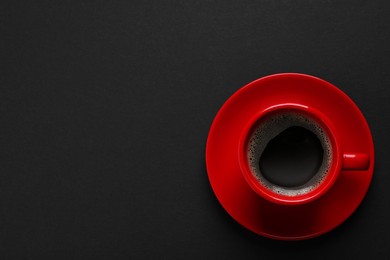 Photo of Red cup with aromatic coffee on black background, top view. Space for text