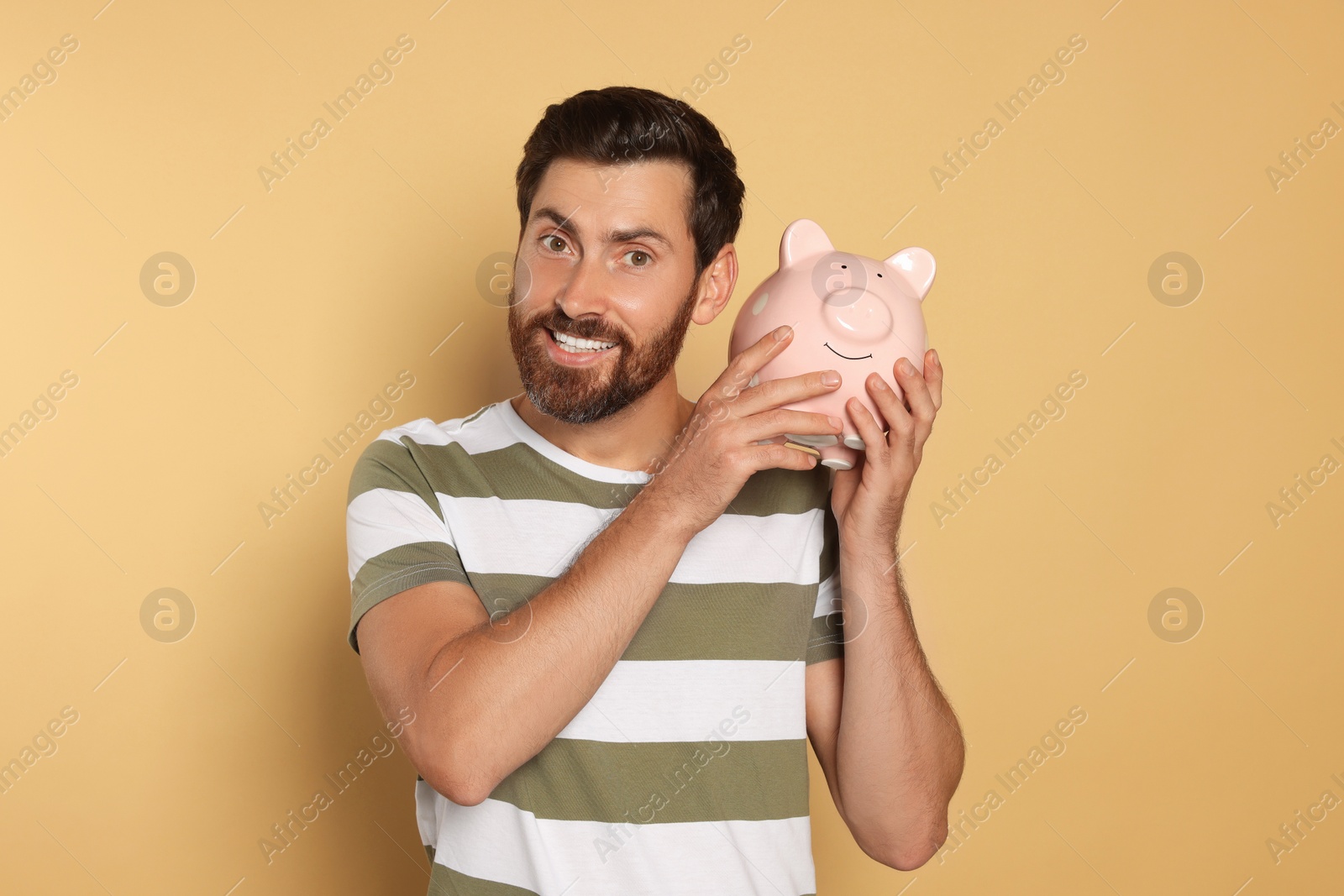 Photo of Happy man with ceramic piggy bank on beige background
