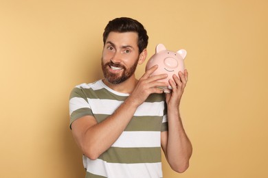 Happy man with ceramic piggy bank on beige background