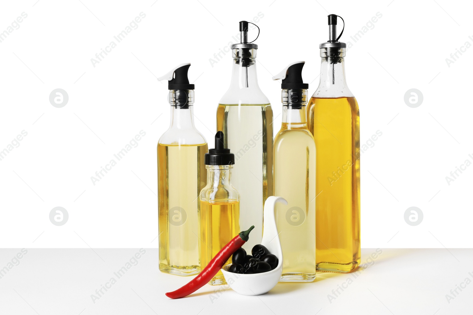 Photo of Bottles of different cooking oils, olives and chili pepper on white background