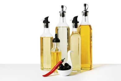 Photo of Bottles of different cooking oils, olives and chili pepper on white background