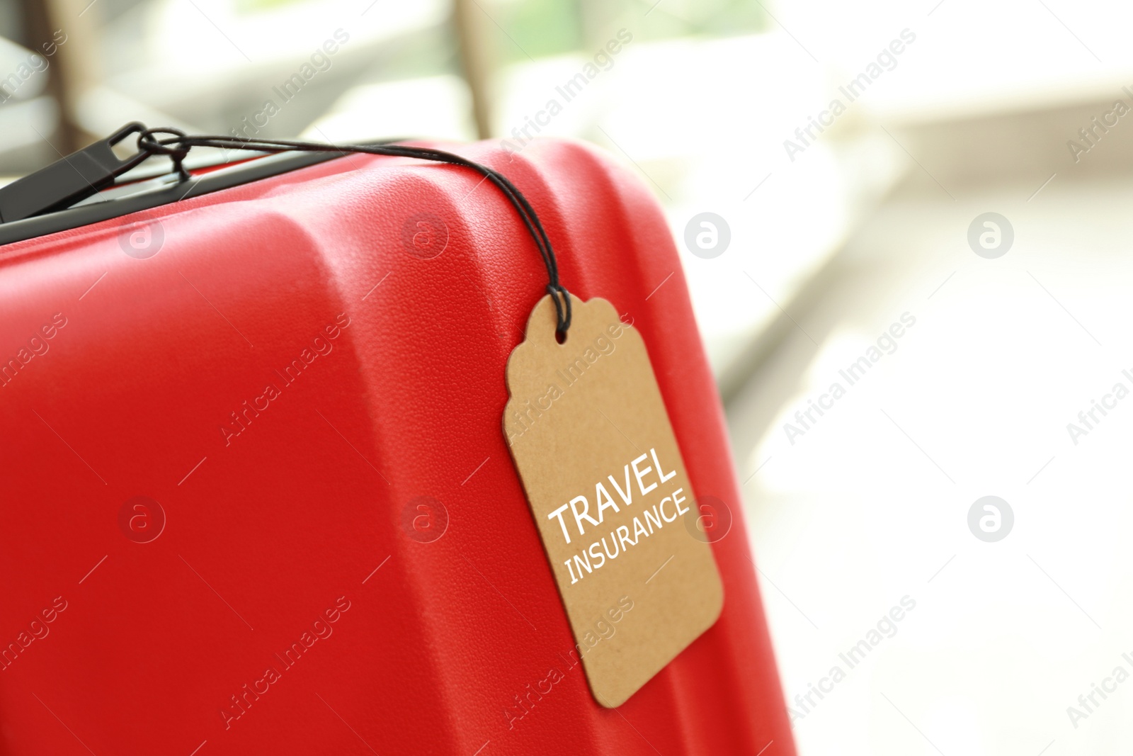 Photo of Red suitcase with TRAVEL INSURANCE label indoors, space for text