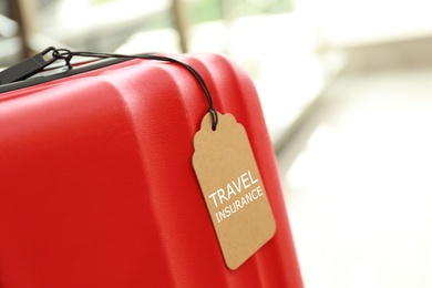 Red suitcase with TRAVEL INSURANCE label indoors, space for text