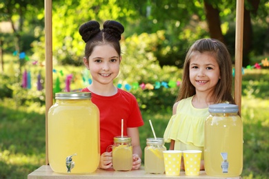 Photo of Cute little girls at lemonade stand in park. Summer refreshing natural drink