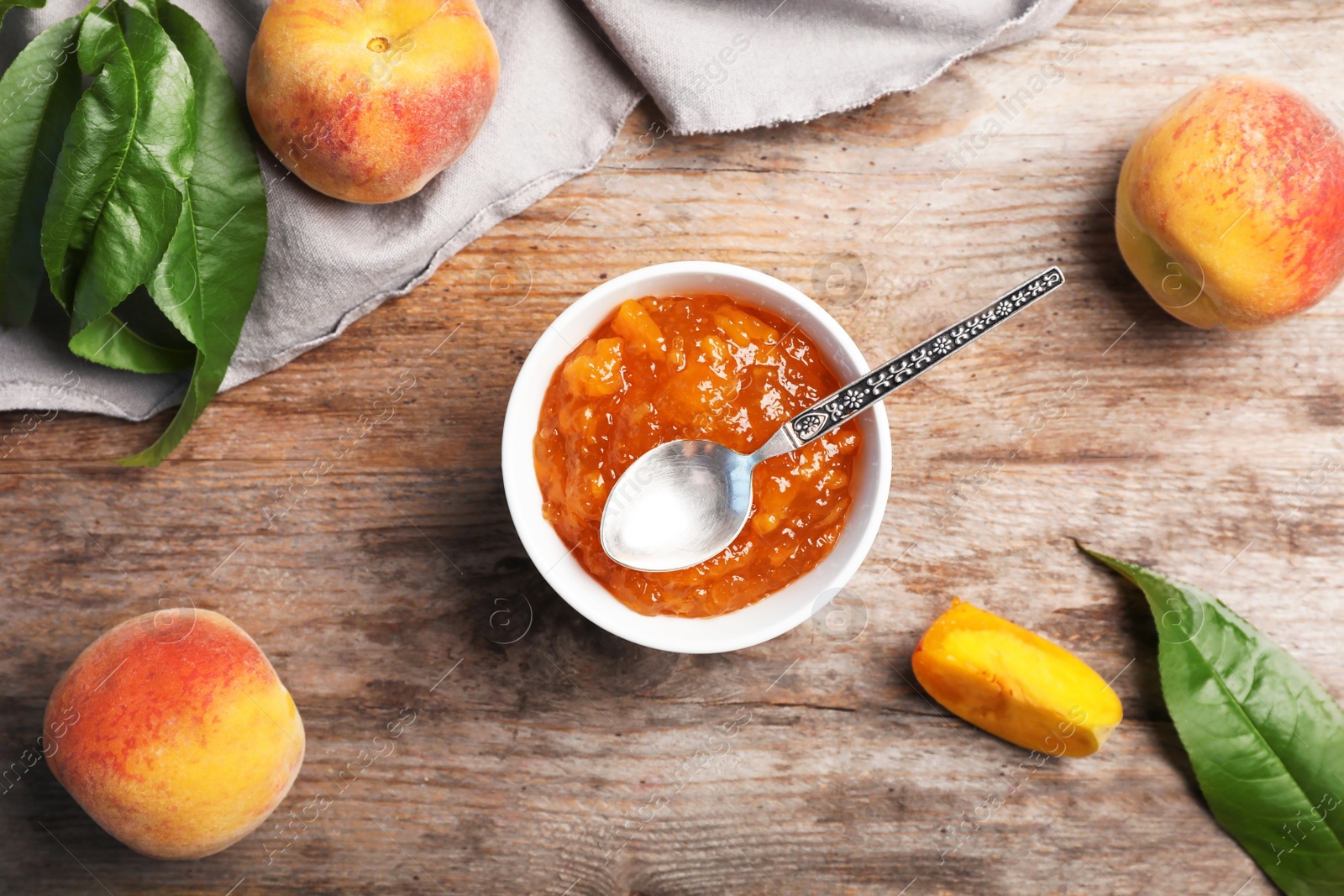 Photo of Flat lay composition with bowl of tasty peach jam, spoon and fresh fruit on wooden table