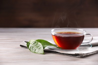 Photo of Aromatic hot tea in glass cup and green leaves on white wooden table. Space for text