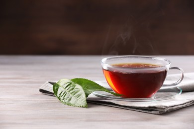 Aromatic hot tea in glass cup and green leaves on white wooden table. Space for text