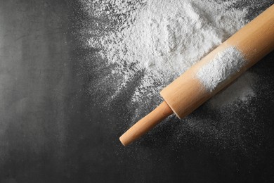 Photo of Scattered flour and rolling pin on black table, top view. Space for text