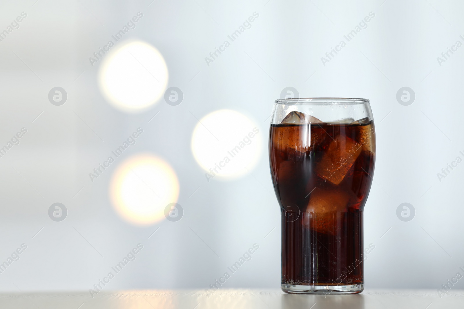 Photo of Glass of cola with ice on table against blurred background. Space for text