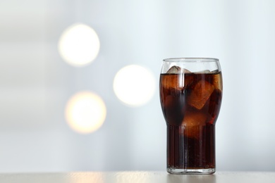 Photo of Glass of cola with ice on table against blurred background. Space for text