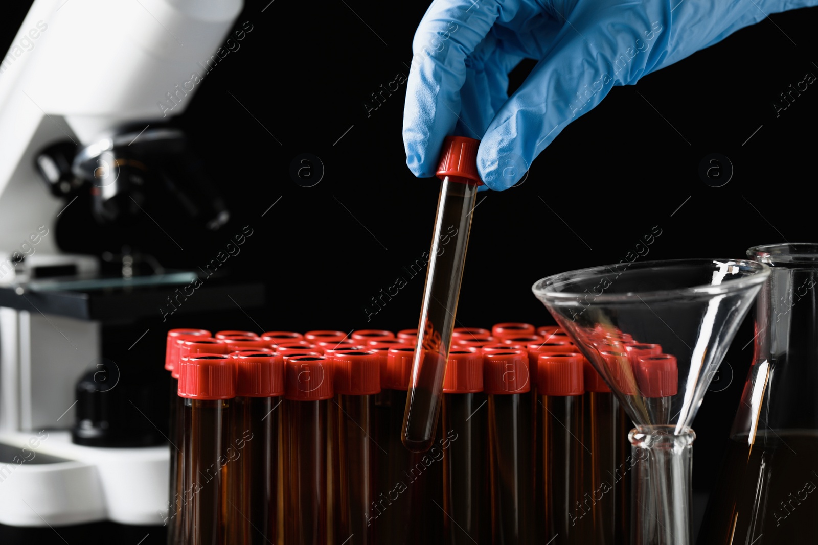 Photo of Scientist taking test tube with brown liquid from stand, closeup