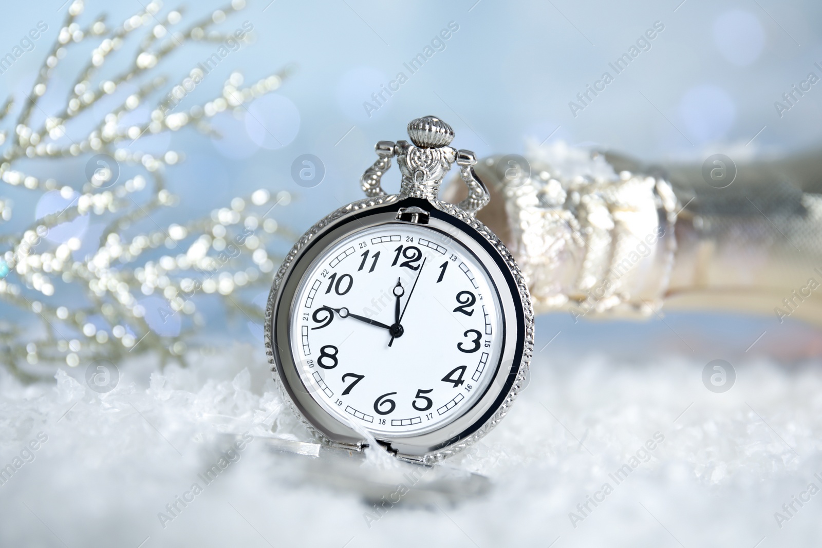 Photo of Pocket watch and bottle of champagne on snow against blurred lights. New Year countdown