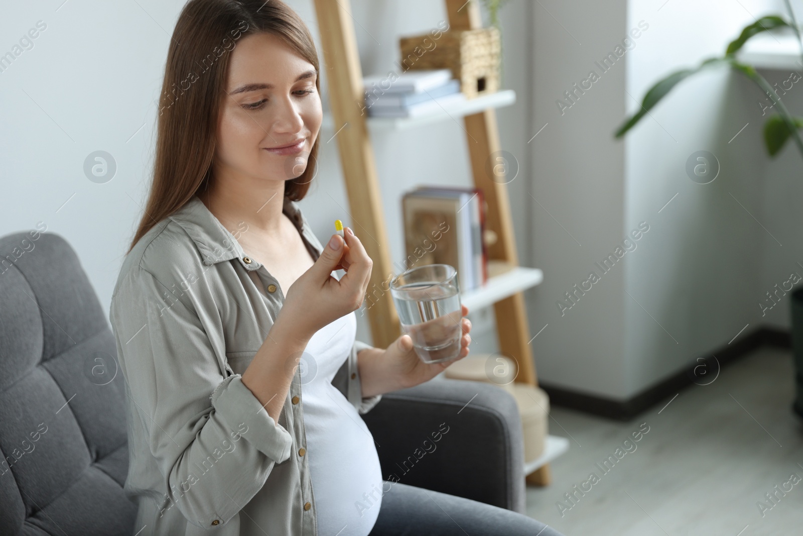 Photo of Beautiful pregnant woman holding pill and glass with water at home