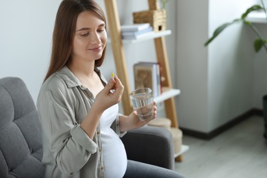 Photo of Beautiful pregnant woman holding pill and glass with water at home