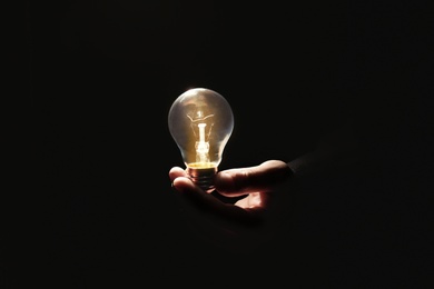 Photo of Man holding modern lamp bulb on dark background, closeup