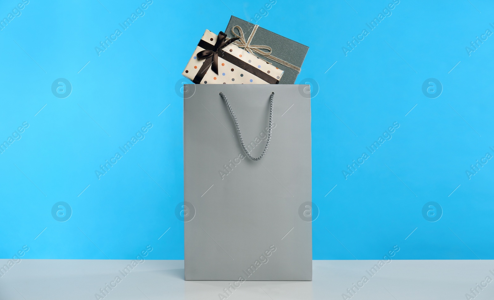 Photo of Paper shopping bag full of gift boxes on light blue background