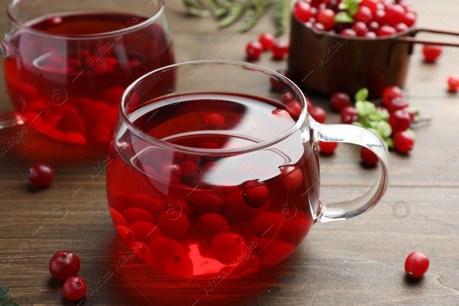 Photo of Tasty hot cranberry tea in glass and fresh berries on wooden table