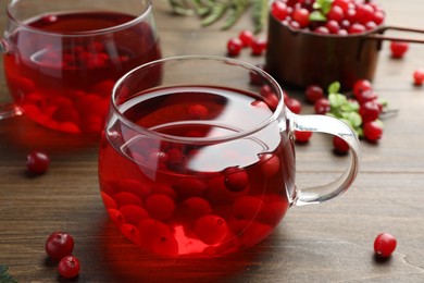 Photo of Tasty hot cranberry tea in glass and fresh berries on wooden table