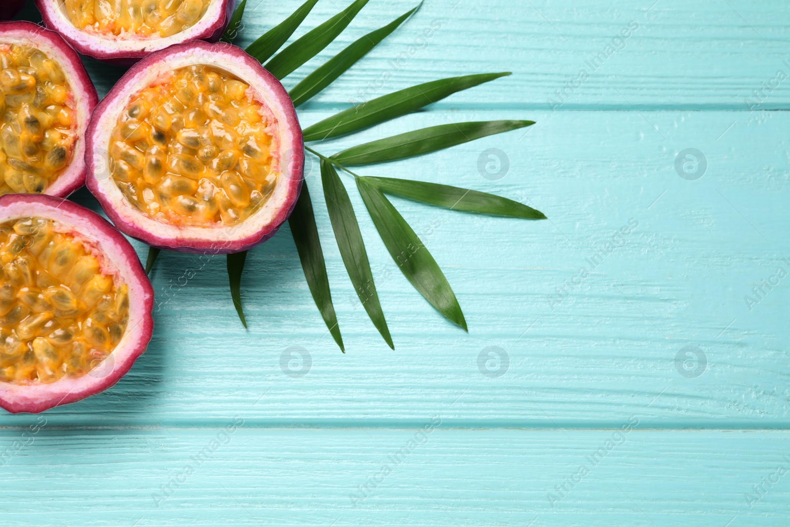 Photo of Halves of passion fruits (maracuyas) and palm leaf on light blue wooden table, flat lay. Space for text