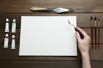 Photo of Man with spatula and blank canvas at wooden table, top view