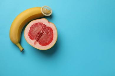Photo of Banana with condom and half of grapefruit on light blue background, flat lay with space for text. Safe sex concept