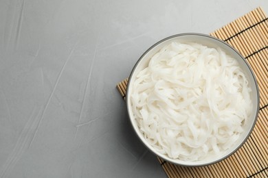 Bowl with cooked rice noodles and straw mat on light grey table, top view. Space for text
