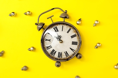 Photo of Alarm clock and festive decor on yellow background, flat lay. New Year countdown