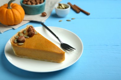 Photo of Piece of delicious pumpkin pie with hazelnuts, seeds and fork on light blue wooden table, space for text