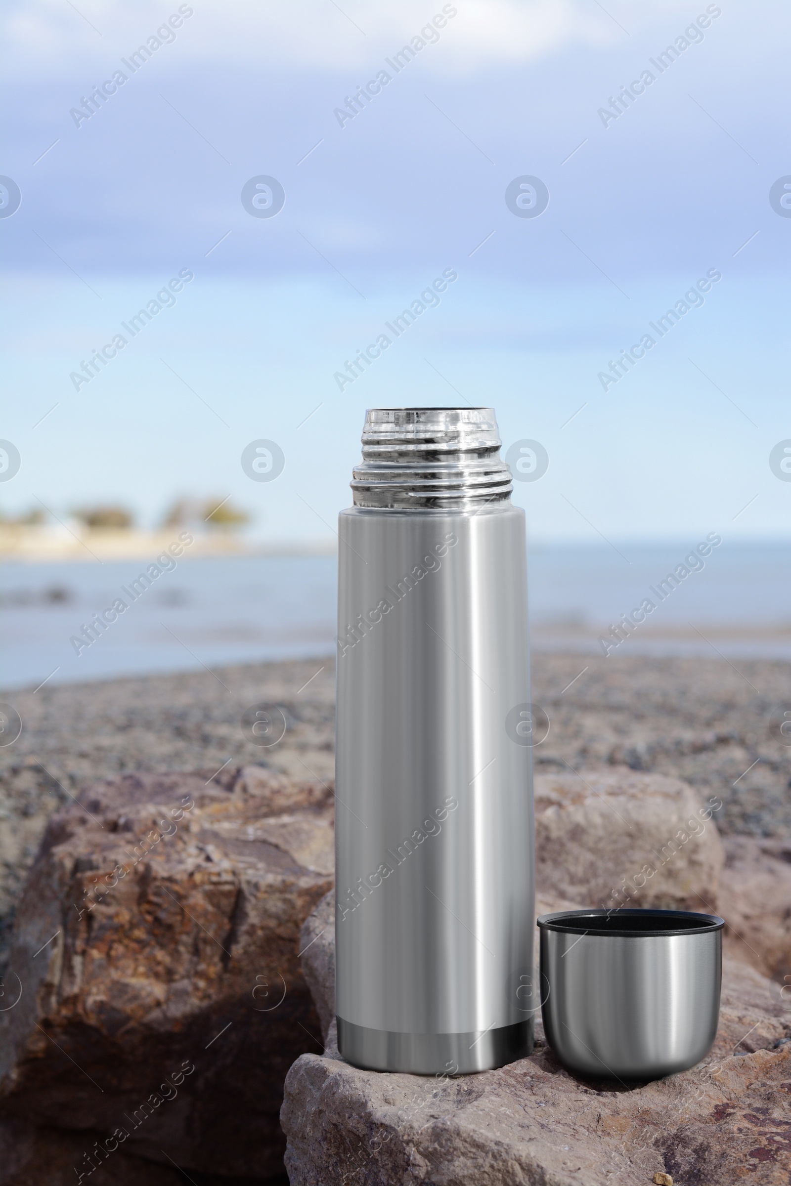 Photo of Metallic thermos and cap on stone near sea
