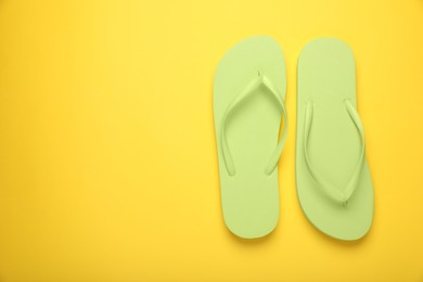 Stylish light green flip flops on yellow background, top view. Space for text