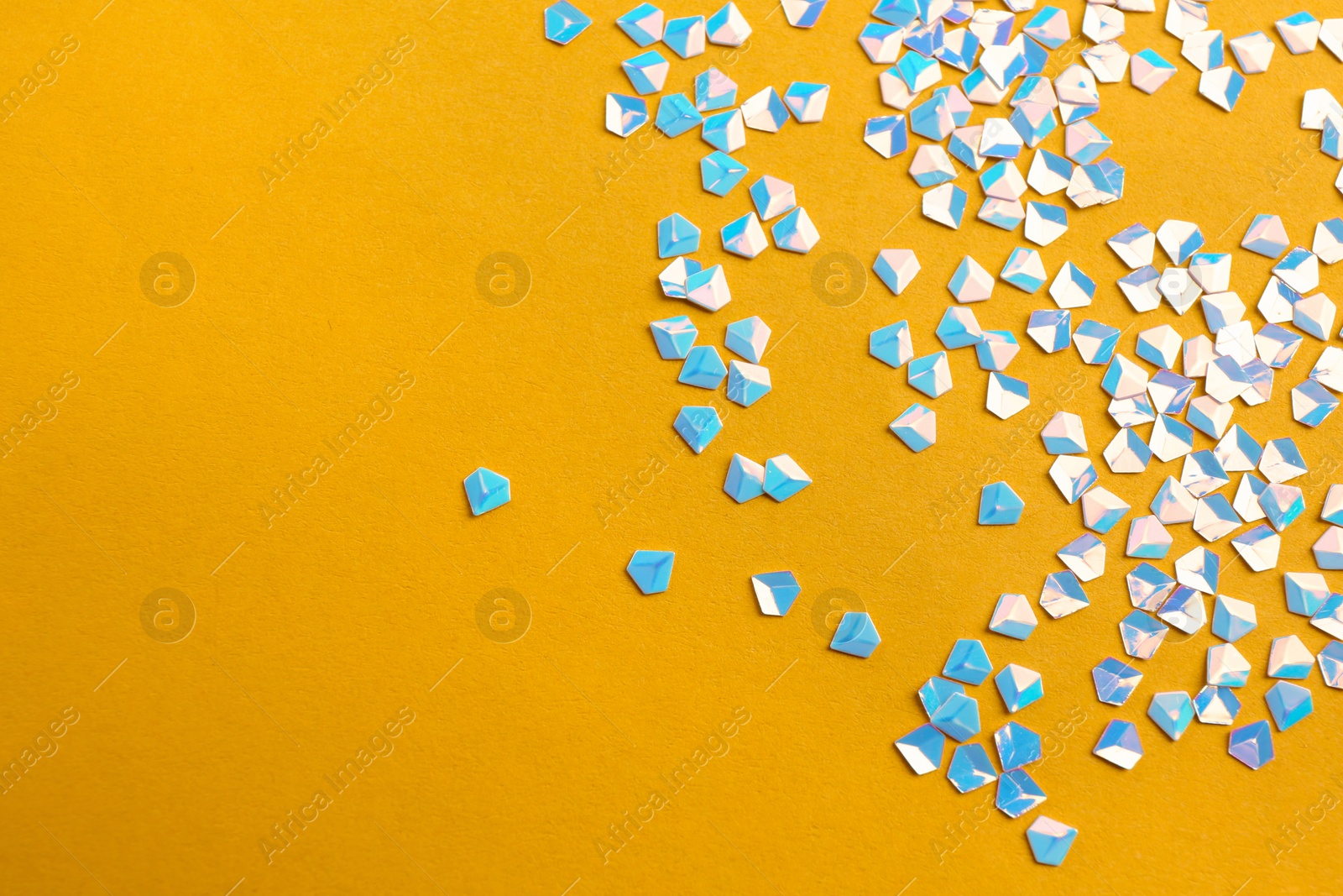 Photo of Shiny bright light blue glitter on yellow background. Space for text