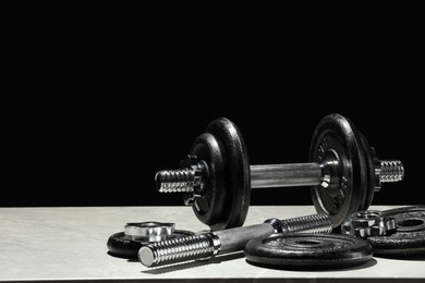 Photo of Barbell and parts of one on light table against black background. Space for text