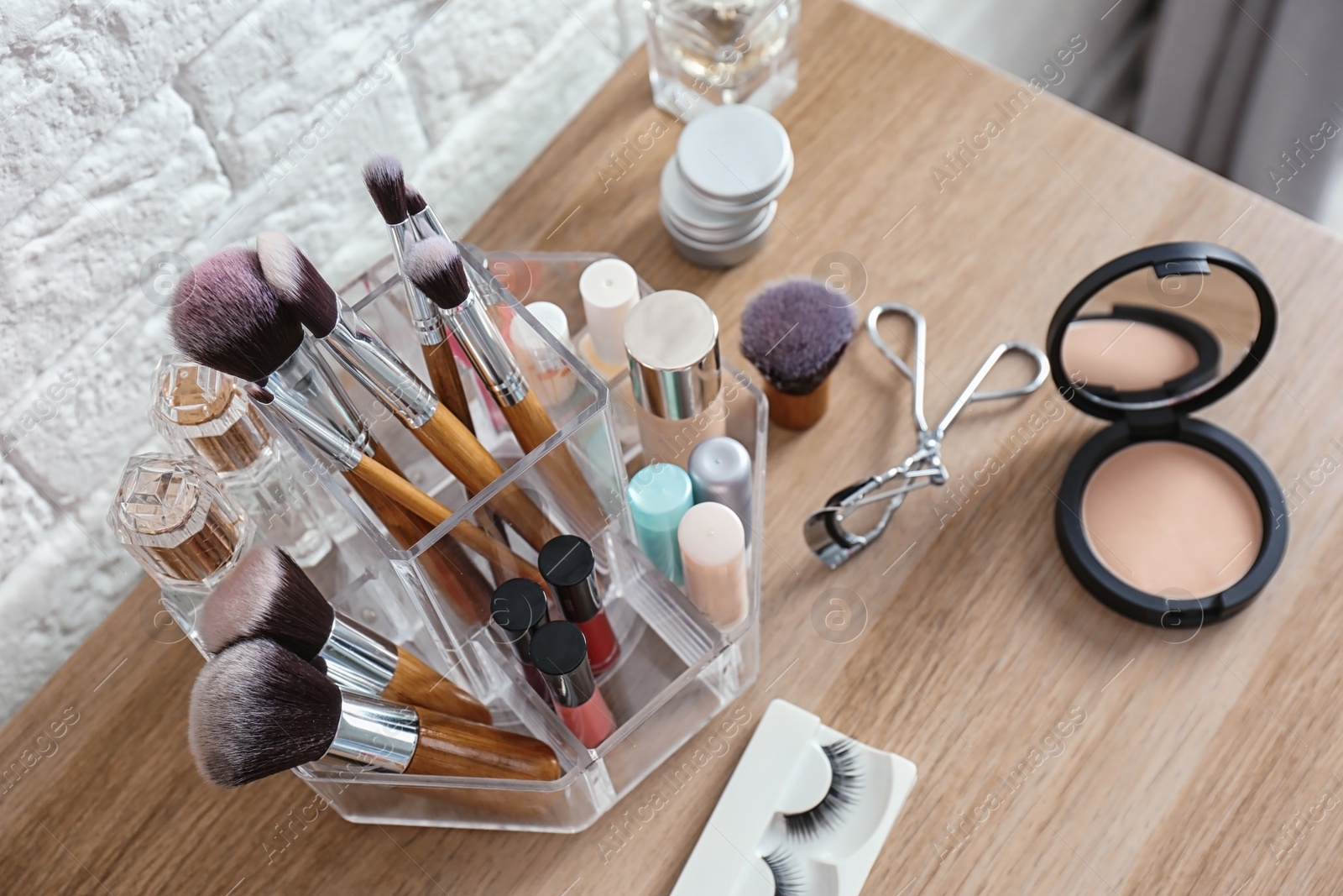 Photo of Organizer with cosmetic products for makeup on table near brick wall