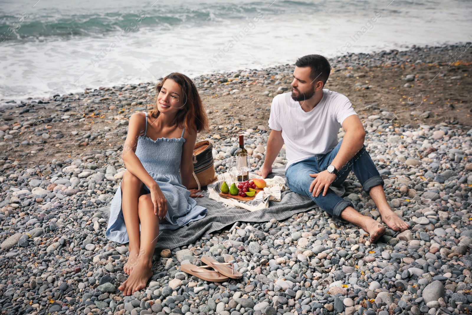 Photo of Young couple having picnic on beach near sea