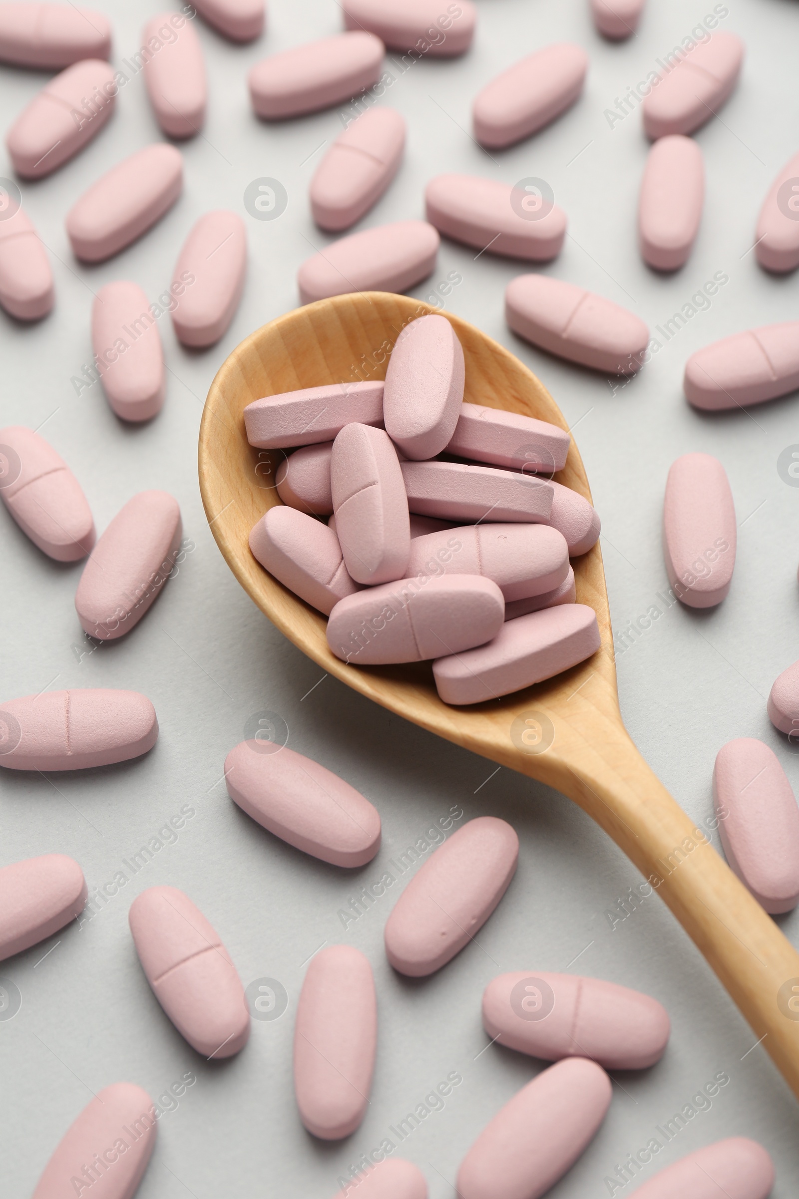 Photo of Vitamin pills and wooden spoon on light grey background, above view. Health supplement