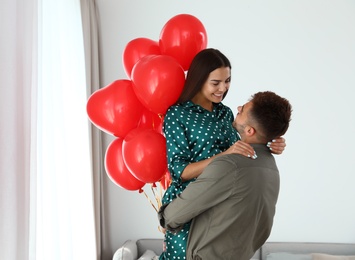 Photo of Young couple with air balloons at home. Celebration of Saint Valentine's Day