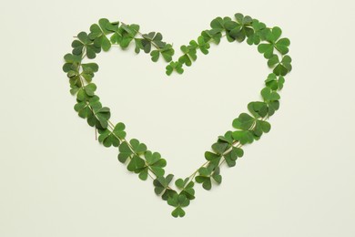Photo of Heart of green clover leaves on light background, flat lay. Space for text