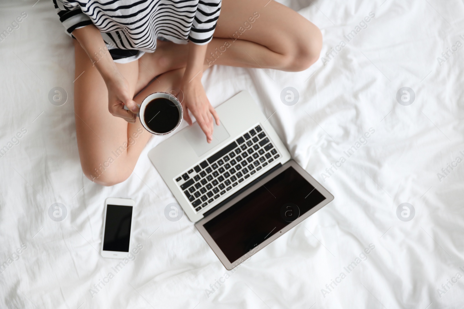 Photo of Female blogger with laptop and cup of coffee on bed, top view