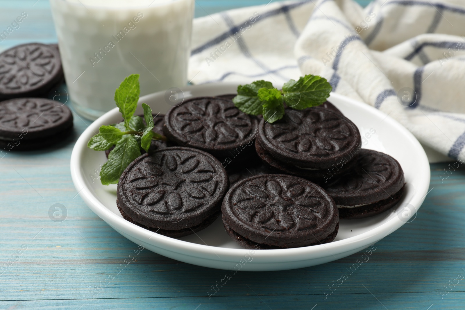 Photo of Plate with tasty sandwich cookies and mint on light blue wooden table, closeup